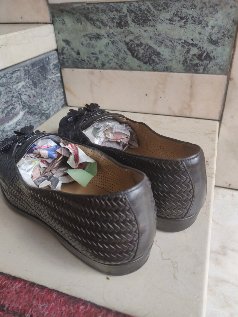 K&ouml;nnte beinhalten: Ein Paar braune Lederschuhe mit gewebtem Muster. Die Schuhe haben Quasten und sind mit zerknittertem Papier gef&uuml;llt.