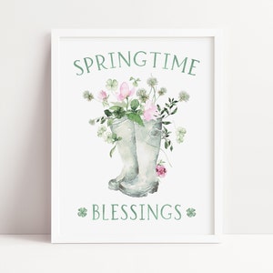 以下が含まれることがあります： 緑色の「SPRINGTIME」と「BLESSINGS」の文字が書かれた白い額縁付きのプリント。灰色のレインブーツがピンクの花と緑のクローバーでいっぱいになっている。