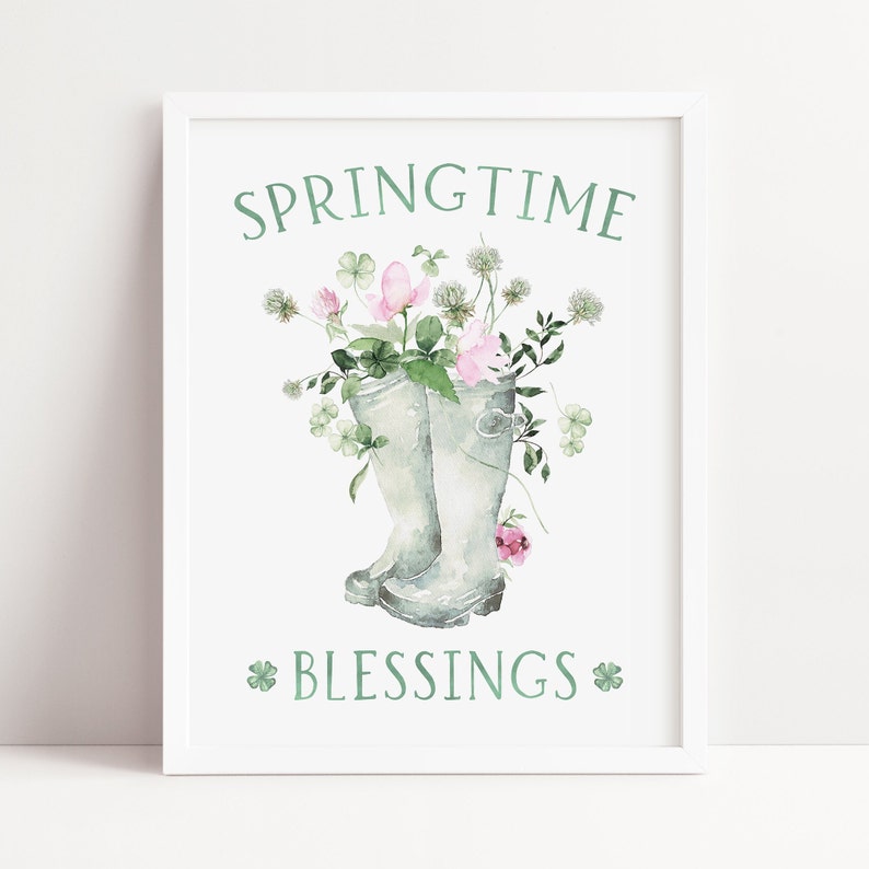 以下が含まれることがあります： 緑色の「SPRINGTIME」と「BLESSINGS」の文字が書かれた白い額縁付きのプリント。灰色のレインブーツがピンクの花と緑のクローバーでいっぱいになっている。