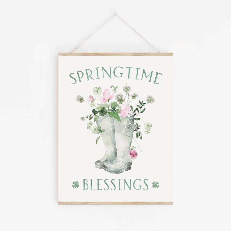 以下が含まれることがあります： 「SPRINGTIME BLESSINGS」と緑色の文字が書かれた白い看板。看板には、ピンクの花と緑の葉がついた緑色のレインブーツ2つが描かれた水彩画が描かれている。