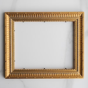 May include: A rectangular picture frame with a metallic gold finish. The frame features a decorative border with repeating vertical ridges and small indentations along the outer and inner edges. Small black metal clips are visible on the inner rim.