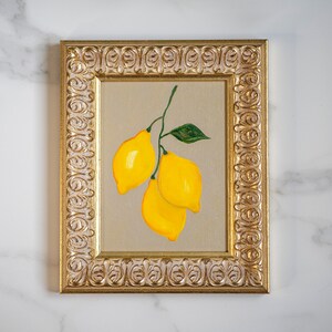 May include: A painting of three yellow lemons with green leaves in a gold ornate frame.