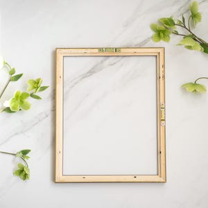 May include: A simple, wooden picture frame with a gold trim sits on a white marble surface. The frame is empty and ready for a photo or artwork.