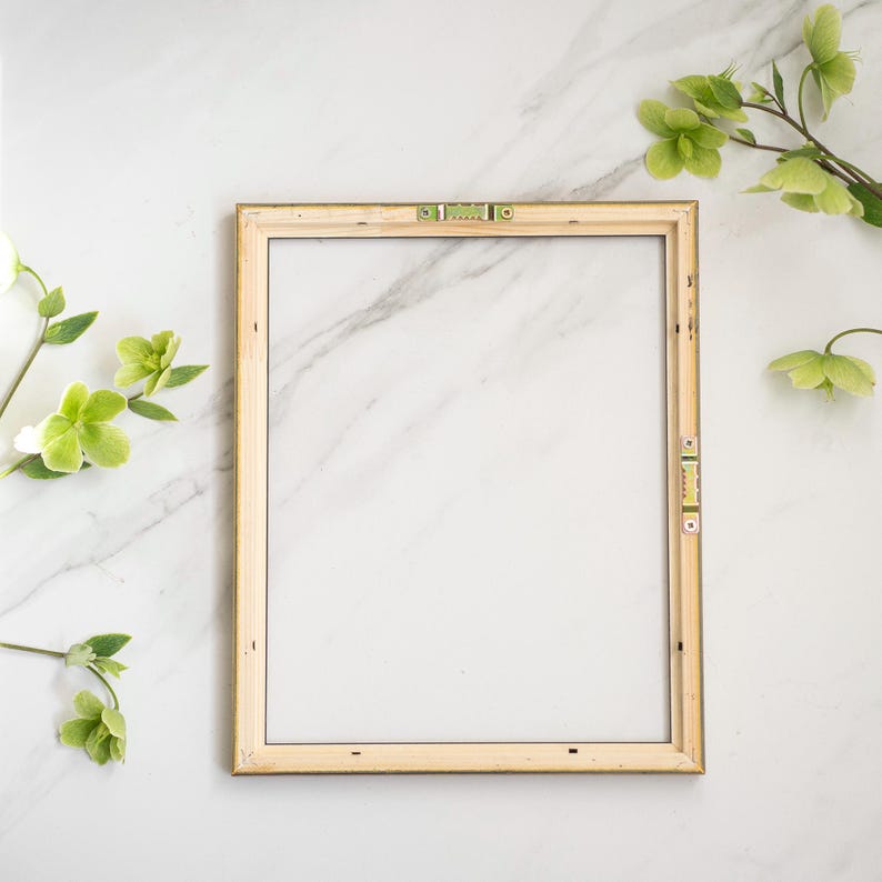 May include: A simple, wooden picture frame with a gold trim sits on a white marble surface. The frame is empty and ready for a photo or artwork.