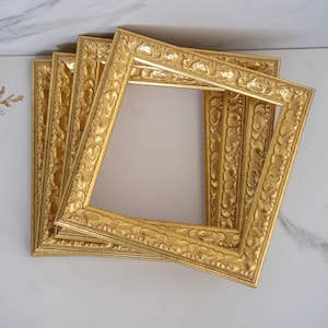 Könnte beinhalten: Vier goldene Bilderrahmen mit verzierten Designs sind übereinander gestapelt. Die Rahmen sind alle gleich groß und haben ein ähnliches Design.