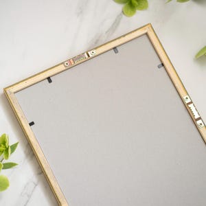 May include: A gold picture frame with a gray backing. The frame has a simple design and is ready to display a photo or artwork.