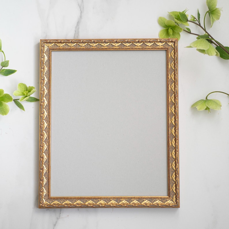 May include: A gold ornate picture frame with a white mat on a marble background.