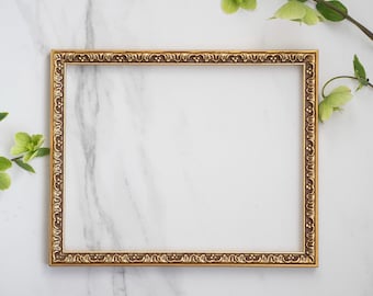 May include: A rectangular picture frame with a metallic gold finish and an ornate, embossed border pattern featuring repeating floral and scroll details. The frame is empty, showcasing a clean, open center space within the decorative molding.