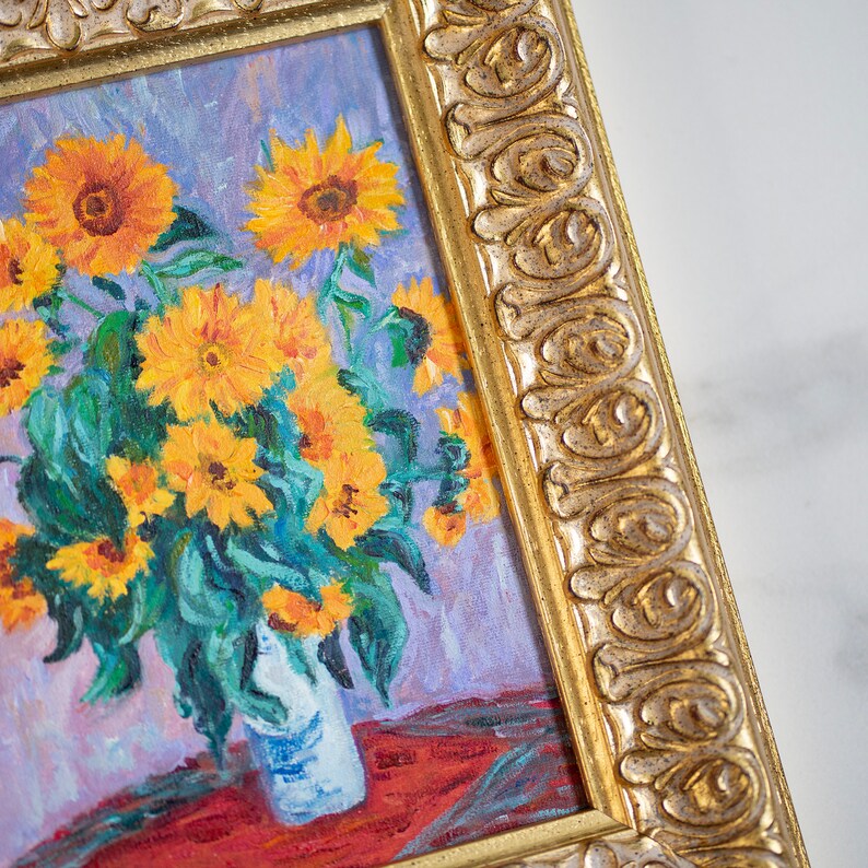May include: A framed oil painting of a bouquet of sunflowers in a vase. The sunflowers are yellow with dark brown centers and green leaves. The vase is white with blue accents. The painting is set against a light purple background.