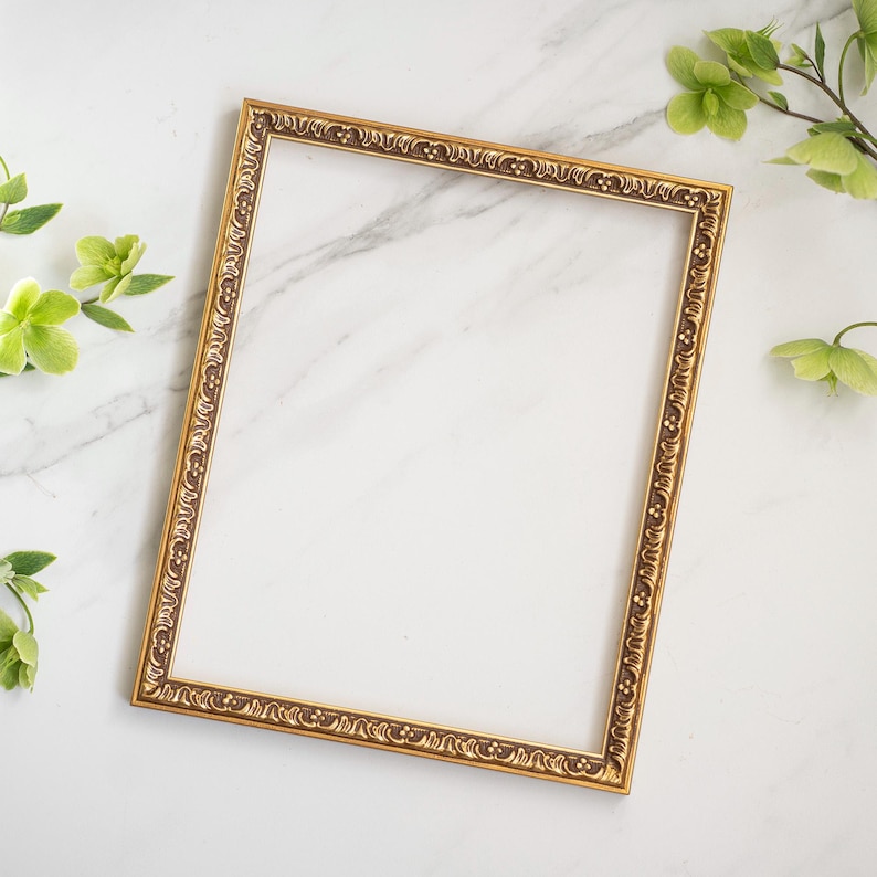 May include: A gold-colored ornate picture frame with a white background. The frame has a decorative design around the edges.