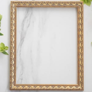 May include: A rectangular picture frame with a metallic gold finish and an ornate, repeating embossed pattern along the border. The frame features a textured, dark-toned inner detail between the raised gold elements, creating a classic look.