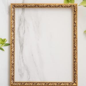 May include: A rectangular picture frame with a metallic gold finish and an ornate, raised relief pattern along the border. The frame features a repeating decorative motif of small circles and curved lines, providing a textured appearance.