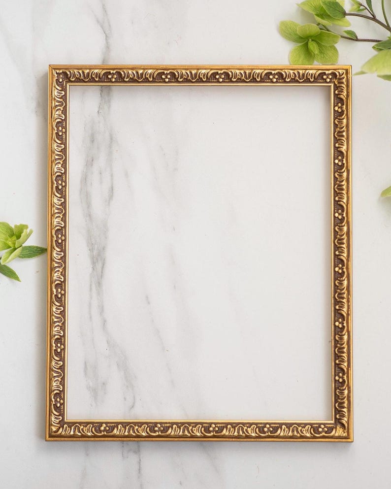 May include: A rectangular picture frame with a metallic gold finish and an ornate, raised relief pattern along the border. The frame features a repeating decorative motif of small circles and curved lines, providing a textured appearance.