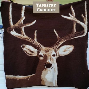 May include: A brown tapestry crochet blanket featuring a white deer with large antlers. The blanket has the text "TAPESTRY CROCHET" at the top.
