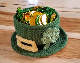 May include: A green crocheted leprechaun hat with a gold buckle and a shamrock design. The hat is filled with gold coins.