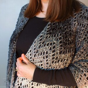 May include: A woman wearing a black long-sleeved shirt with a crocheted shawl in shades of blue, gray, and white.