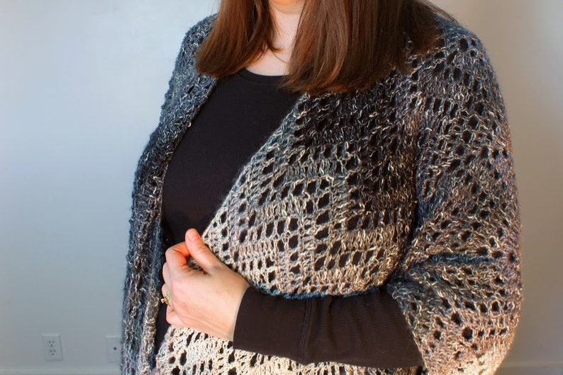 May include: A woman wearing a black long-sleeved shirt with a crocheted shawl in shades of blue, gray, and white.