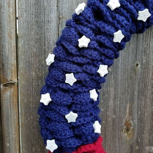 May include: A blue and red crocheted wreath with white star embellishments. The wreath is made of yarn and is decorated with white stars.