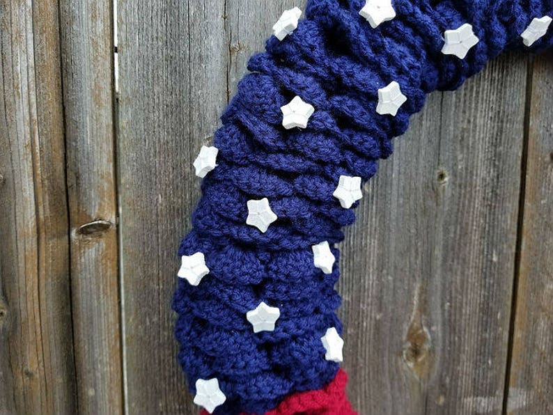 May include: A blue and red crocheted wreath with white star embellishments. The wreath is made of yarn and is decorated with white stars.