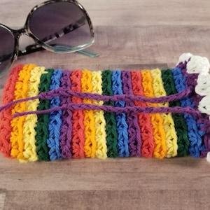Peut inclure: Un étui à lunettes en crochet rayé arc-en-ciel avec une bordure en crochet blanc et des cordons de serrage violets.