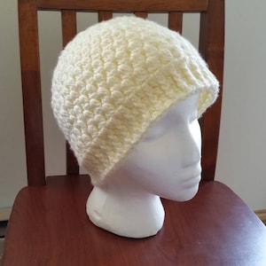 May include: A crocheted beanie in a light yellow color. The beanie is on a mannequin head.