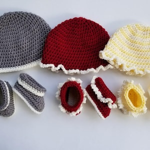 May include: Set of three crocheted hats in gray, red, and yellow with white trim, and six crocheted booties in matching colors with white trim.