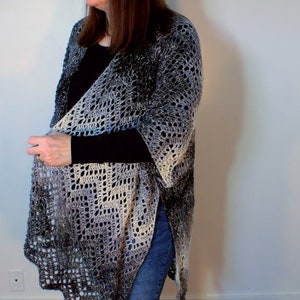 May include: A long, crocheted cardigan in a gradient of blue, gray, and white. The cardigan is open in the front and has a loose, flowing fit.