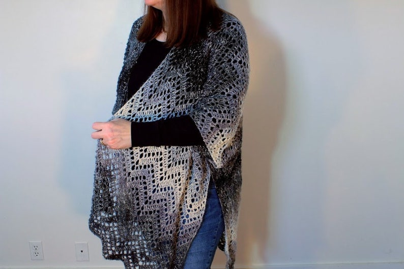 May include: A long, crocheted cardigan in a gradient of blue, gray, and white. The cardigan is open in the front and has a loose, flowing fit.