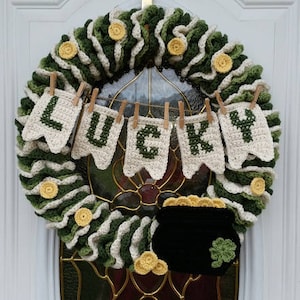 May include: A green and white crocheted wreath with a banner that reads "LUCKY" and a black pot of gold hanging from the bottom.