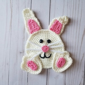 May include: A crocheted white bunny with pink ears, nose, and feet. The bunny has black eyes and a white crocheted nose.