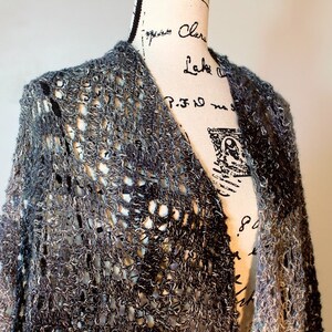 May include: A gray and white crocheted cardigan with a loose, open weave. The cardigan is draped over a dress form.