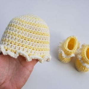 May include: A set of crocheted baby booties and a hat in yellow and white stripes. The booties have a ruffled edge and the hat has a wide brim.