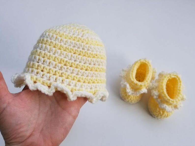 May include: A set of crocheted baby booties and a hat in yellow and white stripes. The booties have a ruffled edge and the hat has a wide brim.