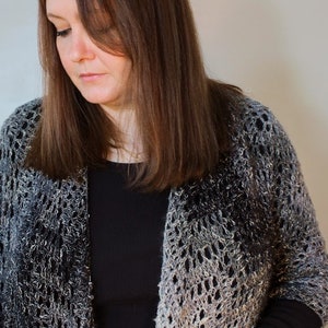 May include: A woman wearing a black top and a silver and black crocheted shawl. The shawl has a lacy pattern and a gradient of color.