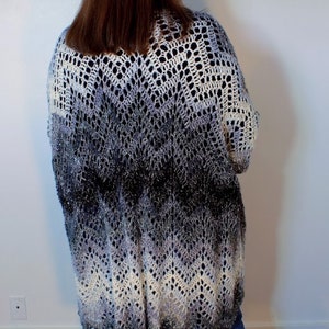 May include: A long, crocheted cardigan in a gradient of white, gray, and black. The cardigan has a loose fit and a delicate openwork pattern.