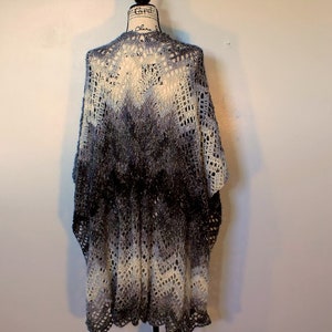 May include: A crocheted shawl with a gradient pattern in shades of white and gray. The shawl has a lacy design and a scalloped edge.