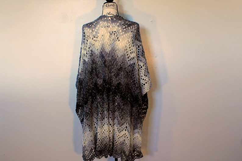 May include: A crocheted shawl with a gradient pattern in shades of white and gray. The shawl has a lacy design and a scalloped edge.
