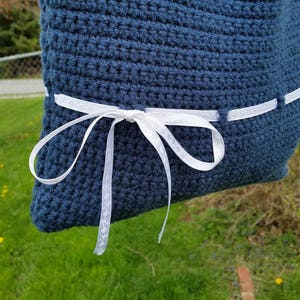 May include: A blue crocheted pillow with a white ribbon tied around it.