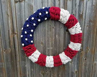 May include: A crocheted wreath in the colors of the American flag, with red, white, and blue yarn. The wreath is decorated with white felt stars.