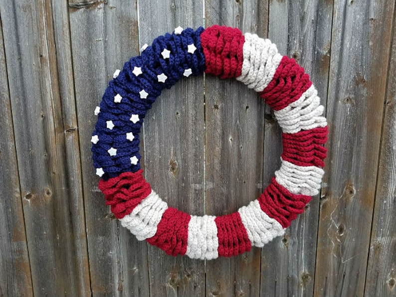 May include: A crocheted wreath in the colors of the American flag, with red, white, and blue yarn. The wreath is decorated with white felt stars.