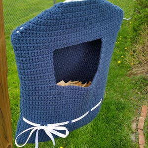 May include: A blue crocheted laundry bag with white ribbon ties. The bag has a large opening at the top and is designed to hold items like socks or small clothing.