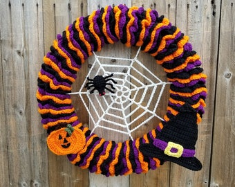 May include: A crocheted Halloween wreath with orange and purple stripes, a white spiderweb with a black spider, a crocheted pumpkin, and a black witch's hat.