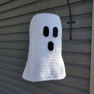 May include: A white crocheted ghost with black felt eyes and mouth hanging from a hook. The ghost is a Halloween decoration.