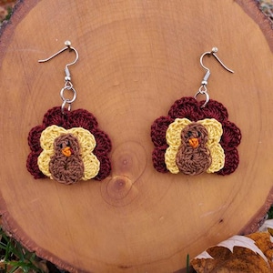 May include: A pair of crocheted turkey earrings with brown, yellow, and orange accents. The earrings are hanging from silver hooks.