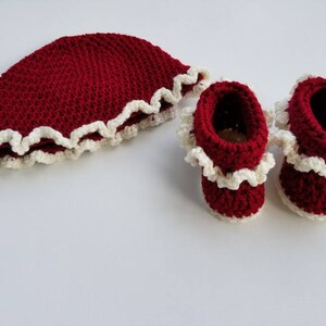 May include: A set of crocheted baby booties and a hat in a deep red color with a white crocheted trim.