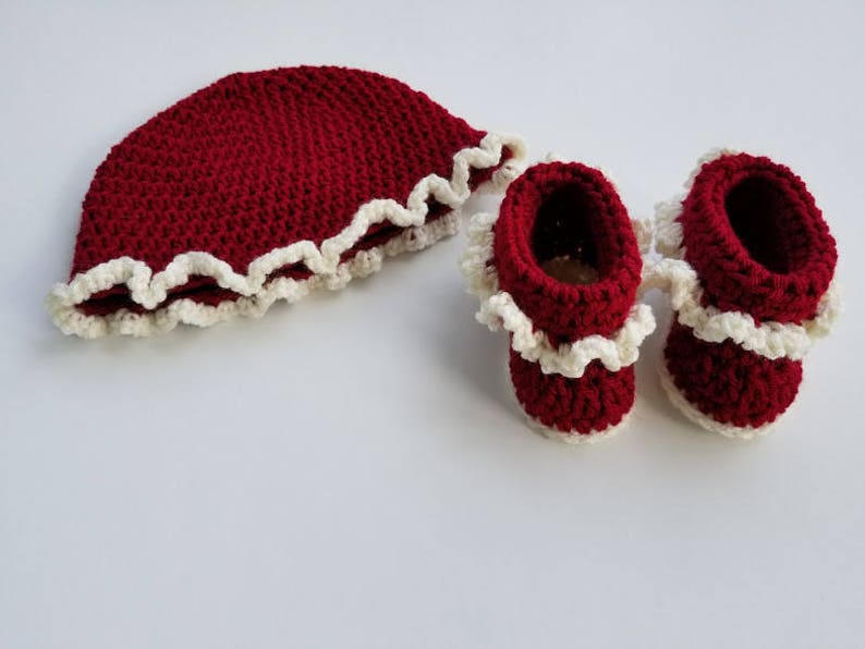 May include: A set of crocheted baby booties and a hat in a deep red color with a white crocheted trim.