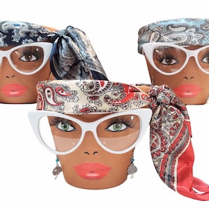 May include: Three terracotta flower pots decorated with painted faces, white cat-eye glasses, and patterned scarves. The faces have long eyelashes and bright red lipstick. One pot has turquoise earrings.