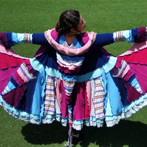 May include: A long, multi-colored cardigan with a ruffled hem. The cardigan is made from a patchwork of different fabrics in shades of pink, blue, and white. The cardigan has a hood and long sleeves.