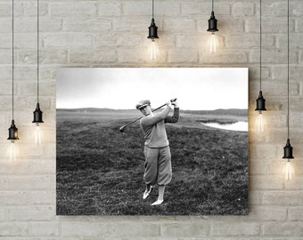 Pode incluir: Fotografia a preto e branco de um golfista com roupa vintage a fazer um swing num campo de golfe. O golfista usa boné, camisola e calças de golfe. O fundo mostra um lago e colinas distantes.