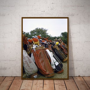 May include: A collection of vintage golf bags in various colors and patterns, including brown, black, and red. Some bags have the text "E.J. Dutch for winner" printed on them.